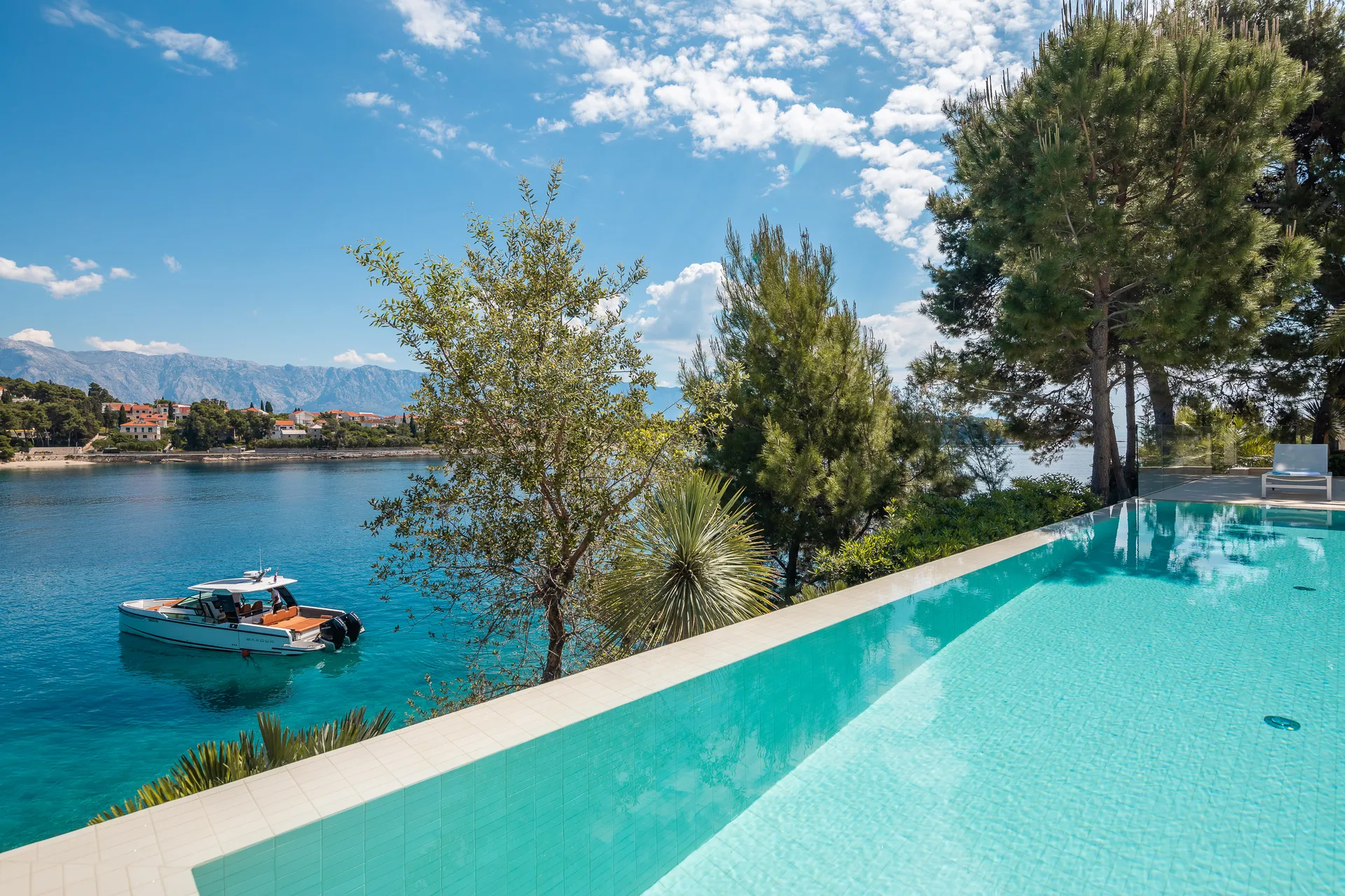 Luxury seafront villa infinity pool looking over a speed boat anchored in a private crystal-clear blue bay.