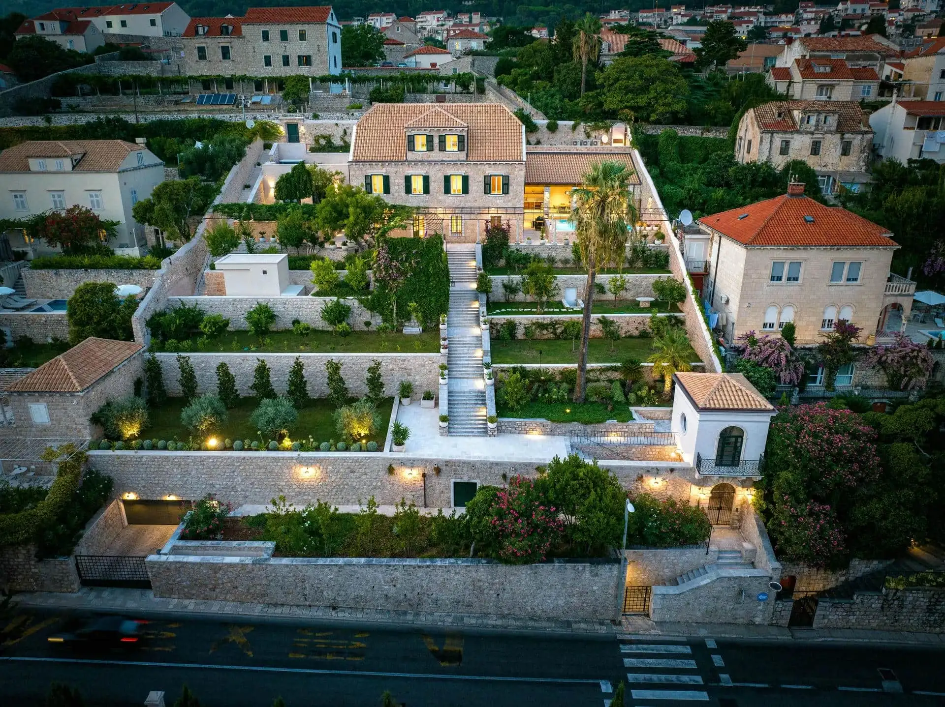 Aerial evening view of a private stone villa in Dubrovnik with terraced gardens, staircase and pool, illustrating the privacy and space of villa rental over a hotel stay
