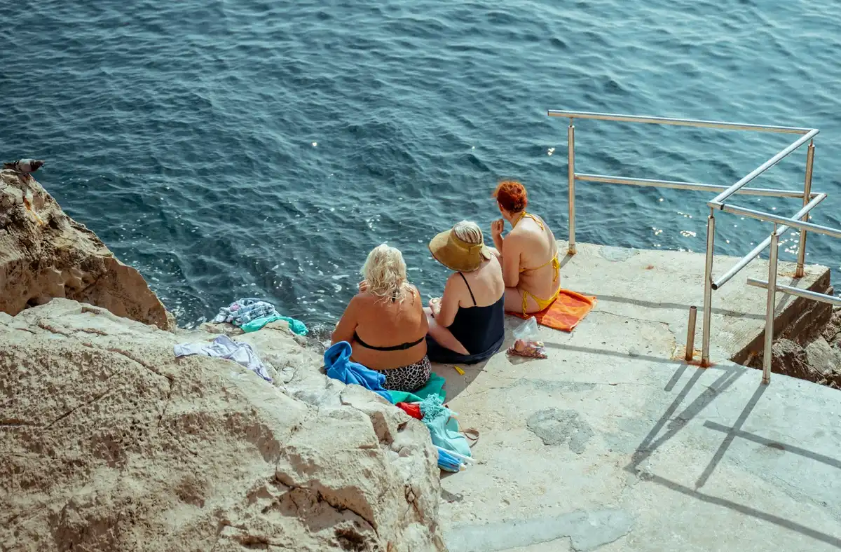 Grandmothers relaxing together on a rocky ledge by the Adriatic Sea during a Croatian family holiday