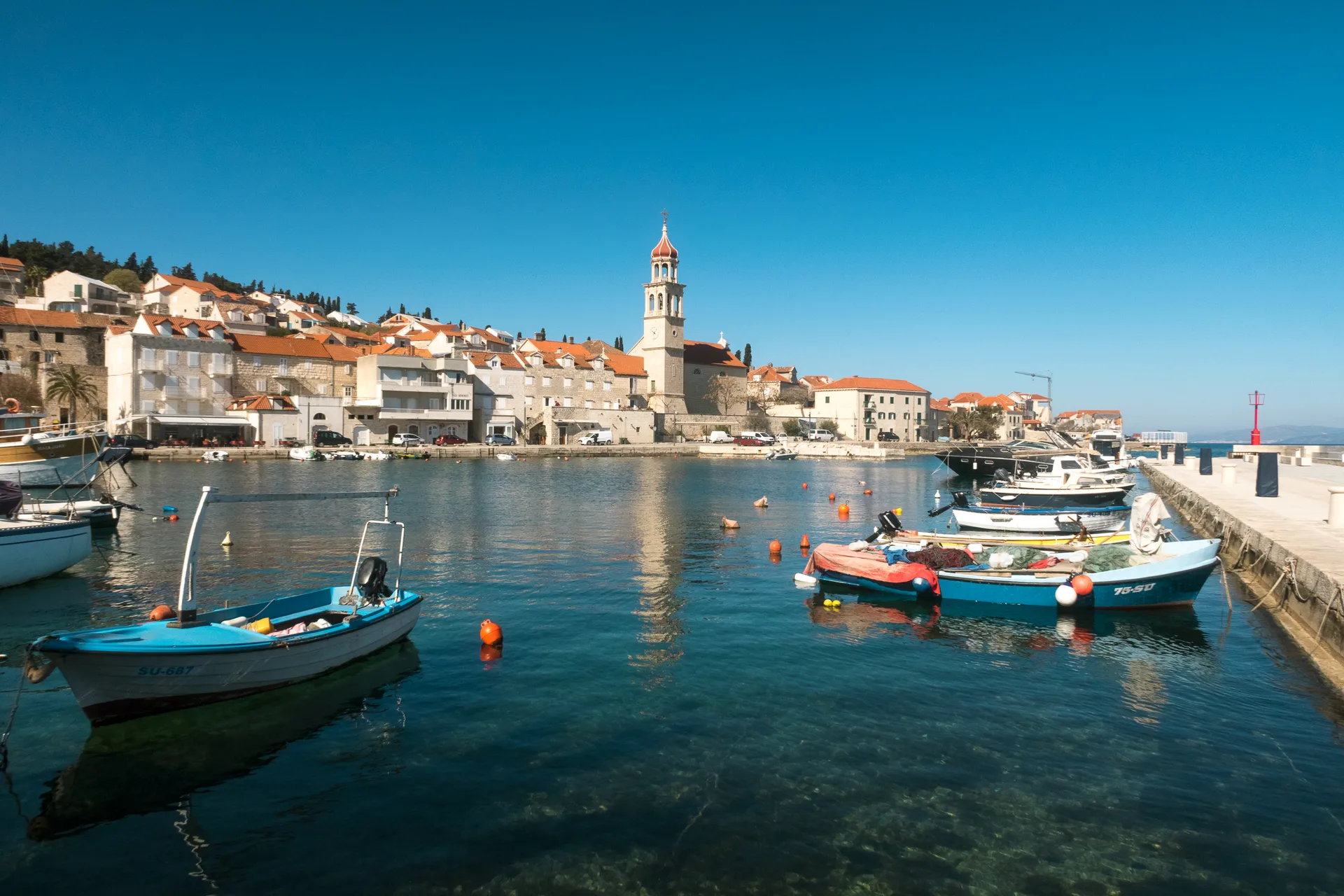Fishing boats moored in Sutivan's small harbor with the village bell tower in the background, Brač