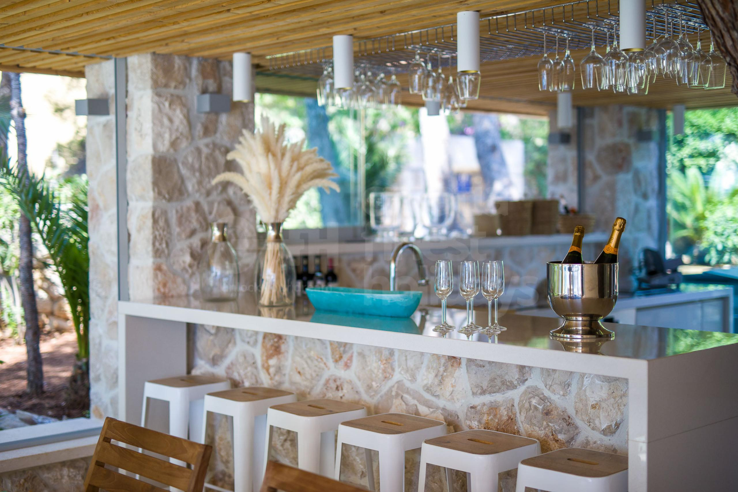 Outdoor kitchen equipped with glasses and a kitchen bar with bar stools