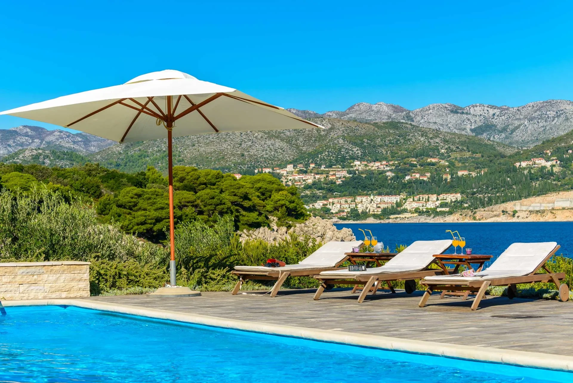 Sun loungers with parasols in front of the luxury Croatia villa Calamota with a pool and private sea deck by the sea