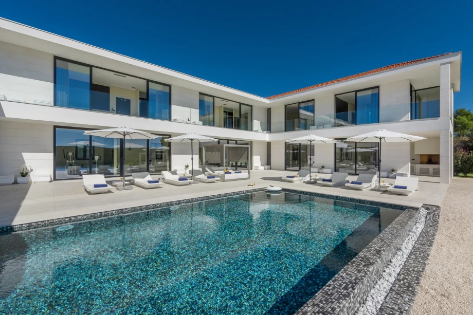 Contemporary villa with a large swimming pool and loungers, set in a serene outdoor environment.