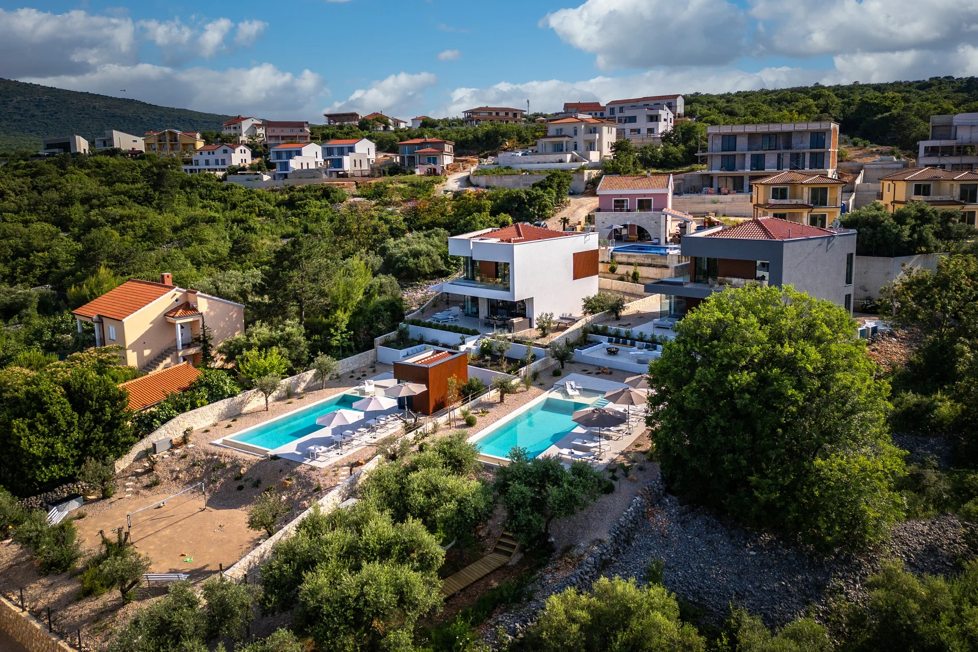 A villa surrounded by lush trees features a sparkling swimming pool in the foreground, creating a serene outdoor retreat.