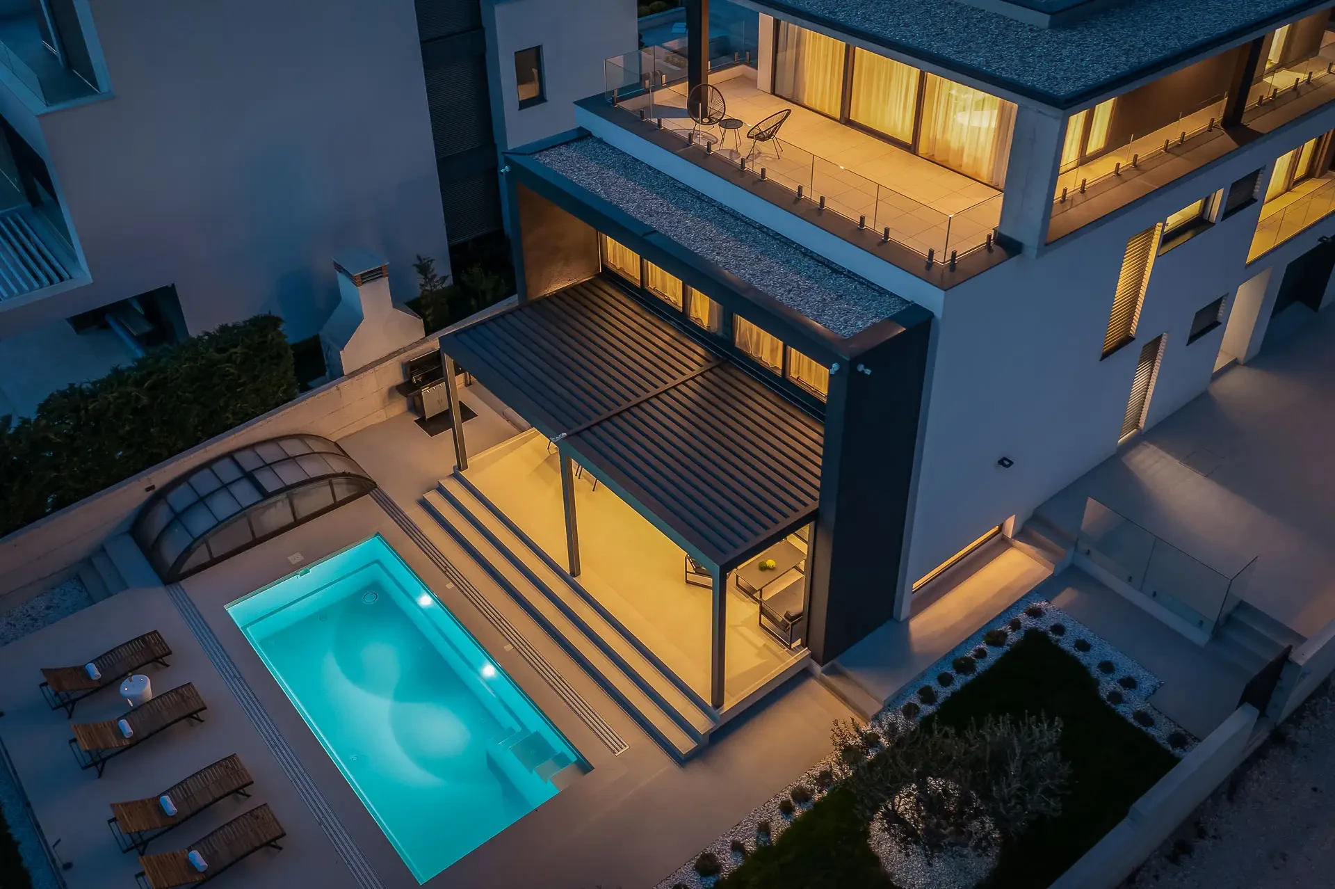 Aerial night view on the outdoor fenced villa area, pool with the patio and sun loungers, main terrace, and bedroom terrace with sitting furniture