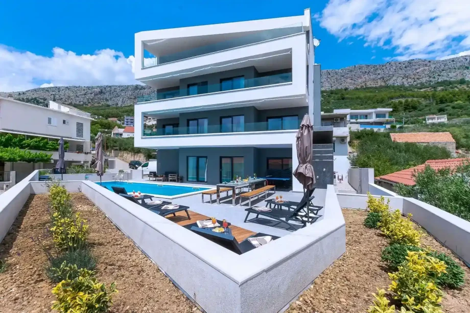 Exterior of luxury family villa Grande Divina with outdoor heated pool, sun loungers, seating area and sea view