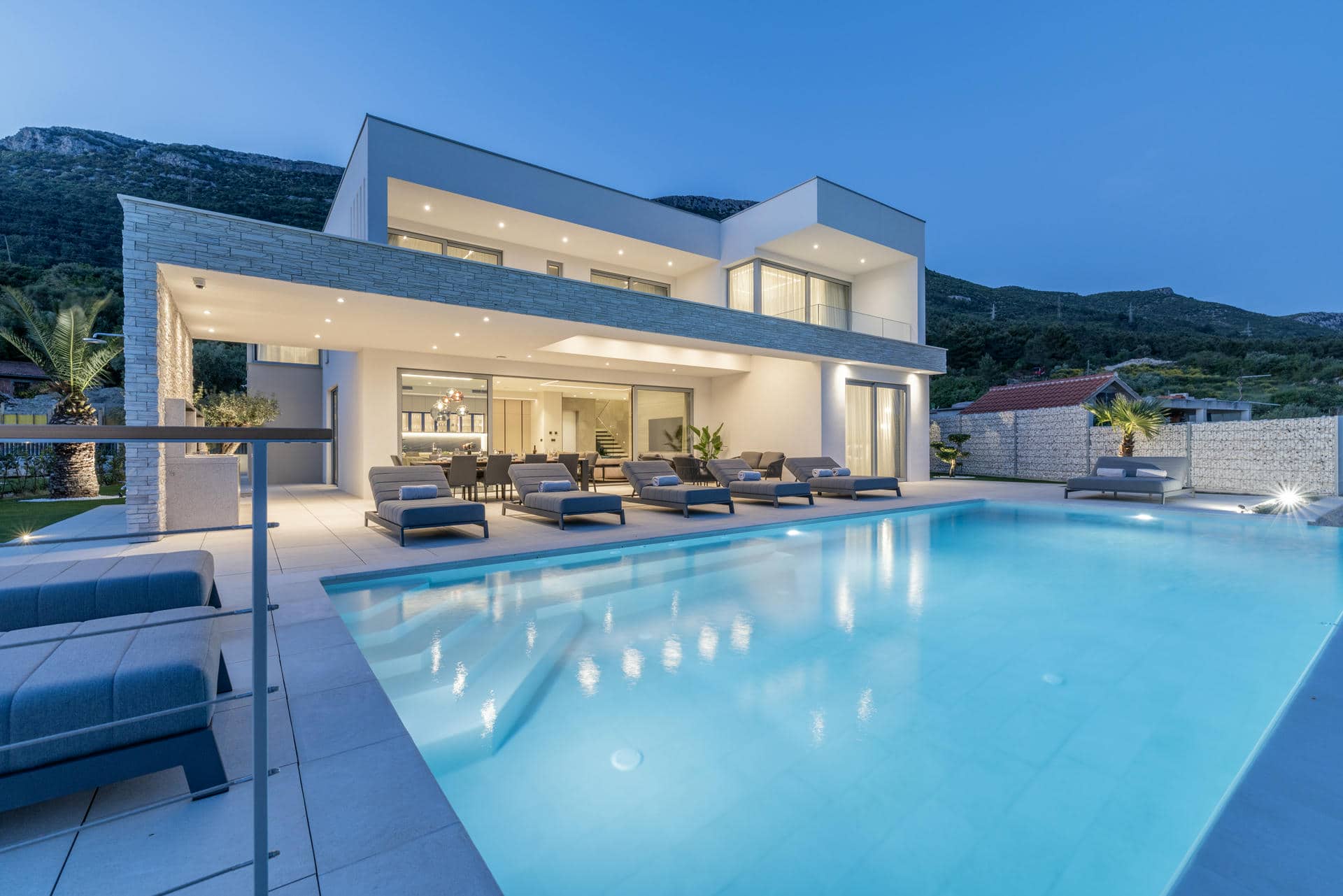 Night photo of modern Villa Nikita in Croatia featuring a sleek design and a big swimming pool surrounded by lush greenery.