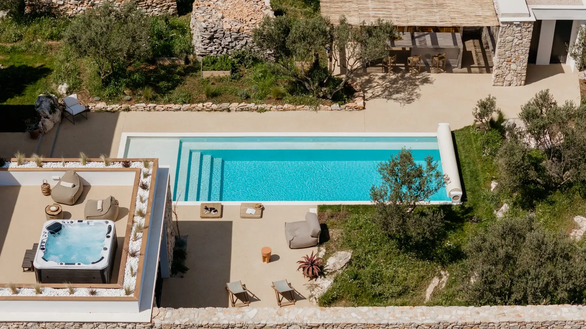 Aerial view of a luxurious villa featuring a sparkling swimming pool surrounded by lush greenery.