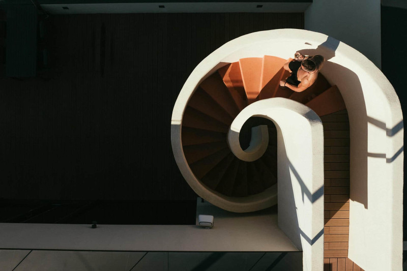 A person sitting on a spiral staircase inside Villa Crispinilla, surrounded by elegant architecture and soft lighting