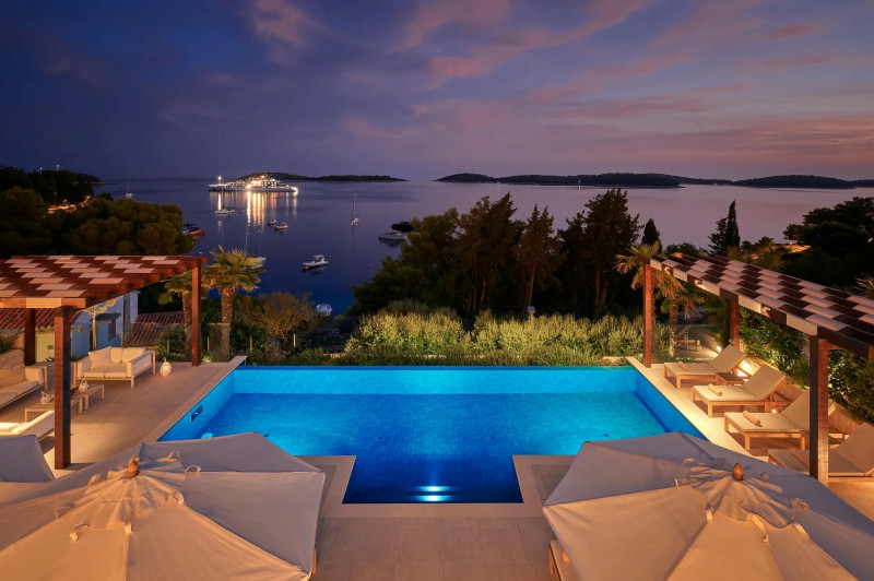 Dusk view of a pool and lounge chairs at Villa Eternal Hvar East, with the sea in the background, evoking relaxation.