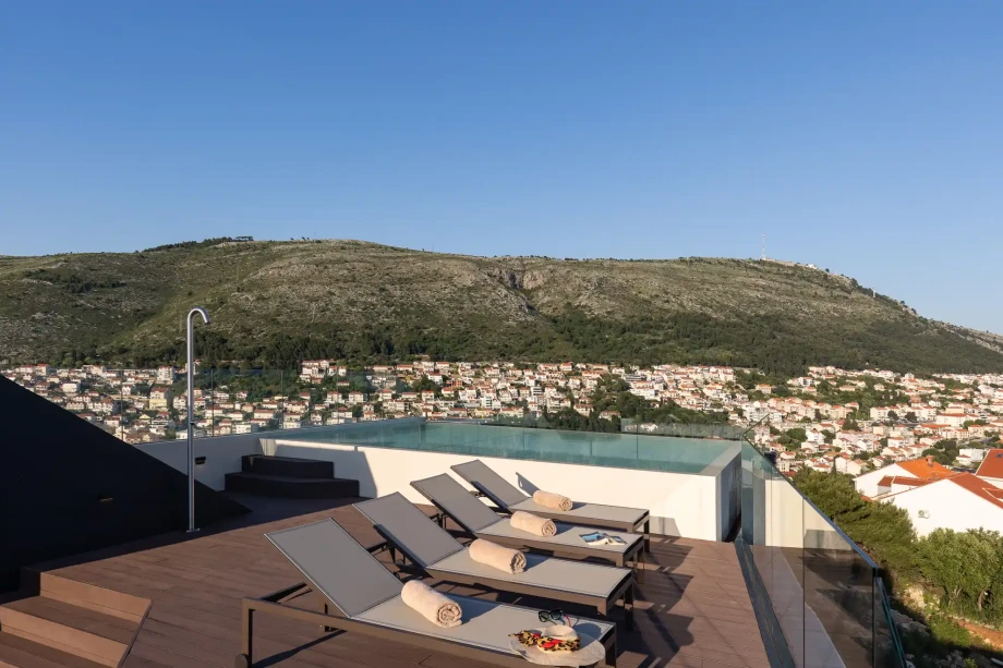 Rooftop pool deck with sun loungers and hillside views above Dubrovnik.