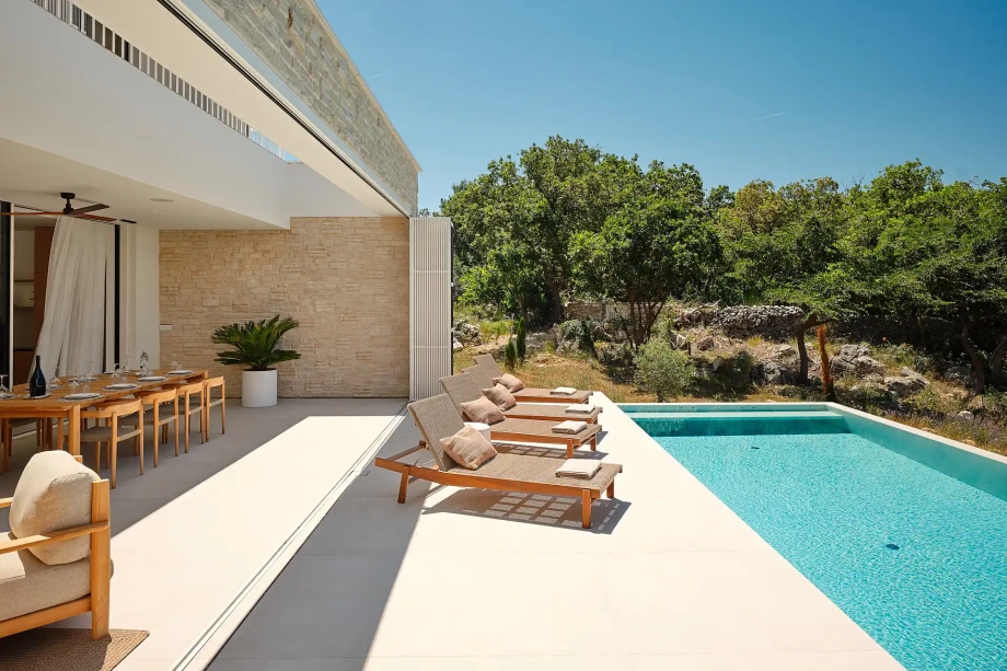Poolside view at a family villa on Pag Island, with lounge chairs and a covered outdoor dining table.