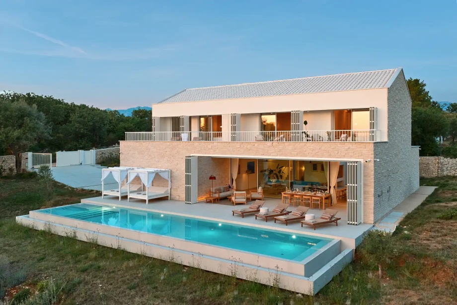 Villa Sunset Novalja with a large  swimmingpool, sun terrace and outdoor seating at dusk.