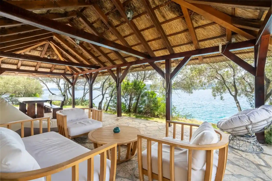 Covered outdoor lounge with wooden furniture overlooking the sea.