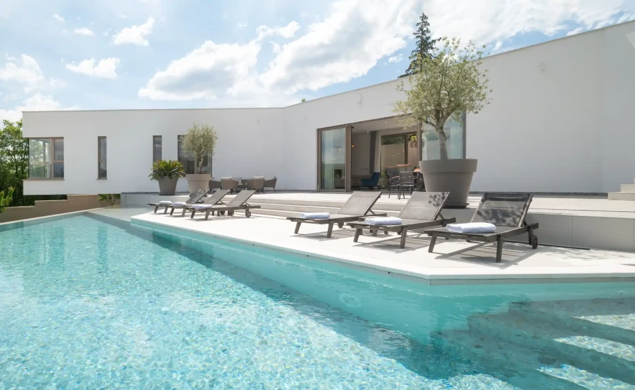 Infinity pool at Villa Imota Sapphire with sun loungers arranged along the terrace and open views toward the surrounding green hills