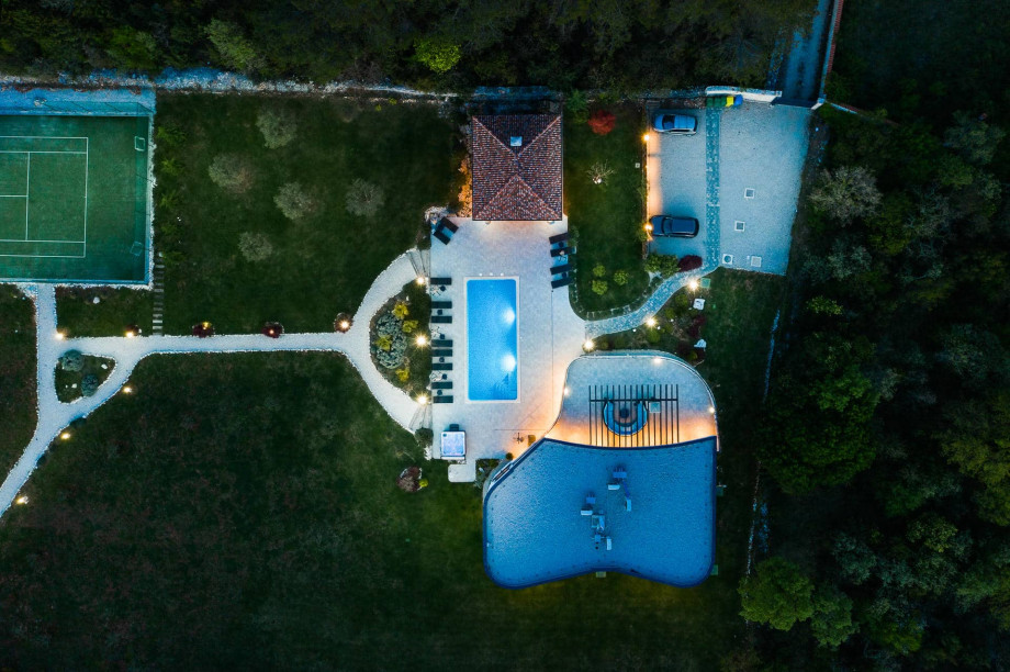 Aerial view of Villa Veradore's grounds at dusk, with pool, a circular seating area, tennis court and parking area